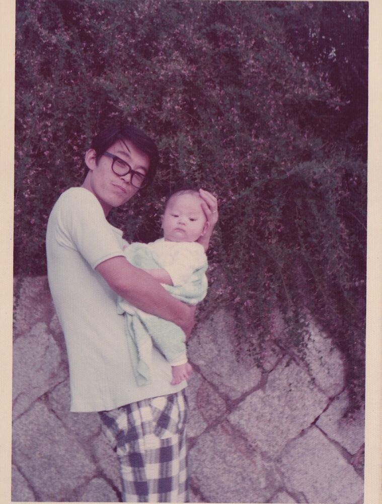 屋外にて、黒ぶち眼鏡をかけたお父様に抱かれる鈴木先生